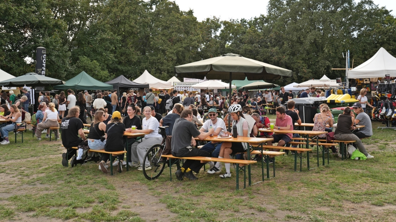 Menschen auf Bierbänken, die ihr Essen beim Veganmania Streetfood Festival genießen.