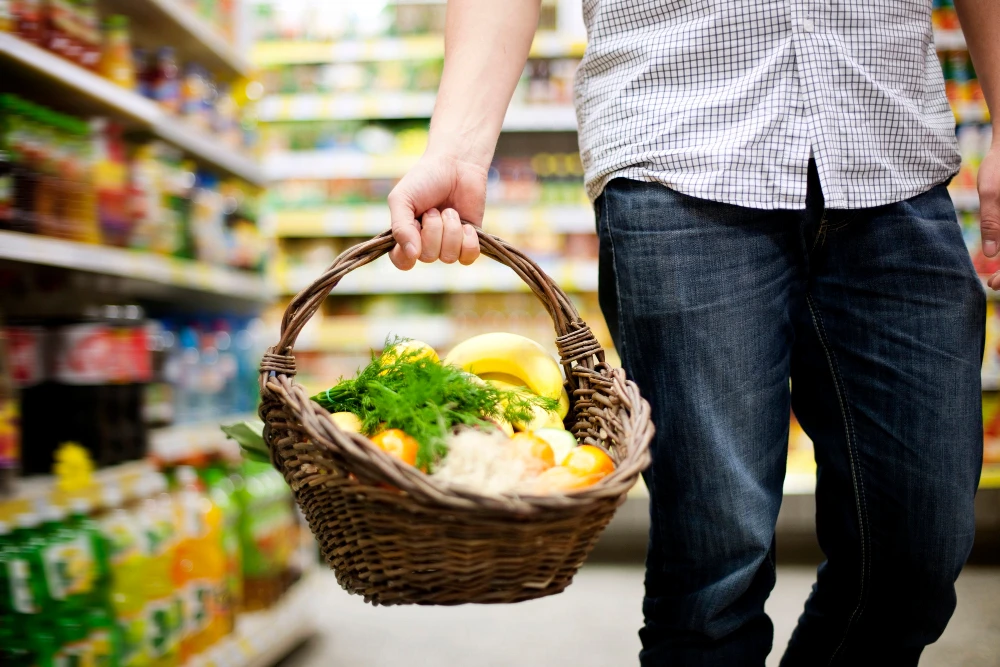 Mann im Supermarkt mit Einkaufskorb, der Gemüse enthält
