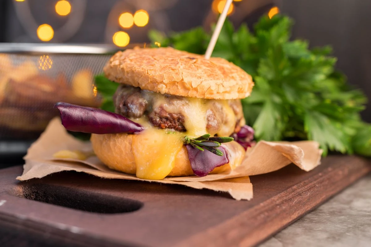Bild eines Cheeseburgers auf einem Holzbrett mit Kräutern und Pommes frites im Hintergrund