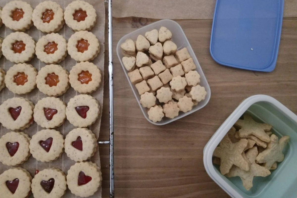 Linzer Augen auf einem Gitte zum Abkühlen, daneben die ausgestochenen "Augen" als zusammengeklebte Kekse und weihnachtliche Sterne