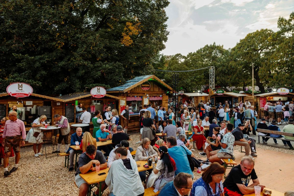 Wiener Wiesn, im Vordergrund Menschen auf Heurigenbänken, im Hintergrund mehrere Hütten mit Essensständen