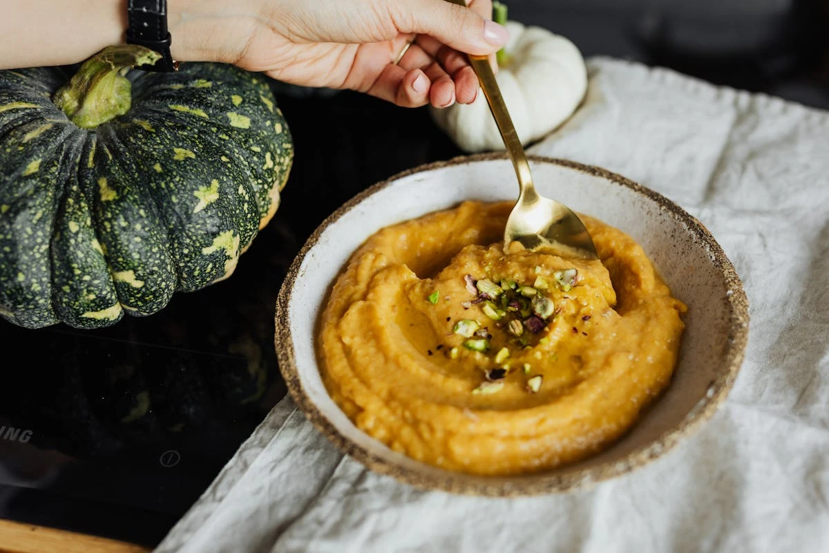 Kürbissuppe mit gehackten Kürbiskernen, im Hintergrund ein grüner Kürbis